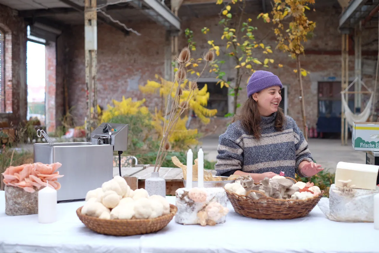 Emmi an einem Markttisch mit Pilzen in der Backsteinhalle der Glasfabrik